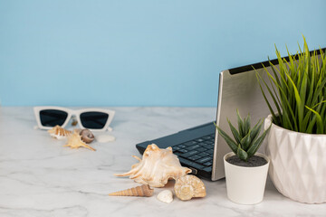 Laptop on a blue background with greenery, shells and sunglasses. The concept of remote work for programmers, designers, freelancers. Sea work and recreation, online education. Copy space for text