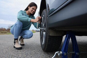 Fototapeta na wymiar Young woman changing tire of car outdoors