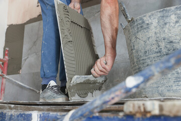 Worker applying cement on wall tile for installation indoors, closeup