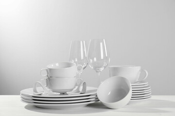 Set of clean dishware and glasses on white wooden table against light background