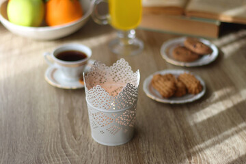 Cup of tea, plates with cookies, glass of orange juice, books, reading glasses, bowl of fruit and candles on the table. Selective focus.