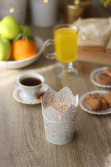 Cup of tea, plates with cookies, glass of orange juice, books, reading glasses, bowl of fruit and candles on the table. Selective focus.