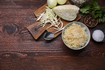 Bowl of tasty sauerkraut and ingredients on wooden table, flat lay. Space for text
