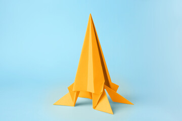 Origami art. Handmade yellow paper rocket on light blue background