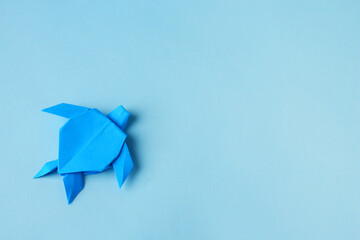 Origami art. Handmade bright paper turtle on light blue background, top view with space for text