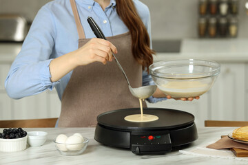 Woman cooking delicious crepe on electric maker at white marble table in kitchen, closeup