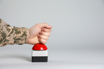 Serviceman pressing red button of nuclear weapon on light gray background, closeup with space for text. War concept