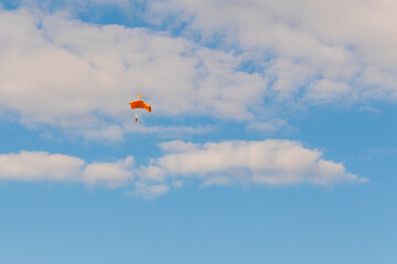 Skydiver, parachutist flying with parachute against blue sky with white clouds at Air Show. Parachuting sport, extreme and leisure activity concept