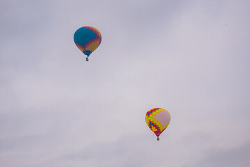 Two colorful hot air balloons flying against grey sky at Winter aerostat festival. Freedom, sport, aircraft concept