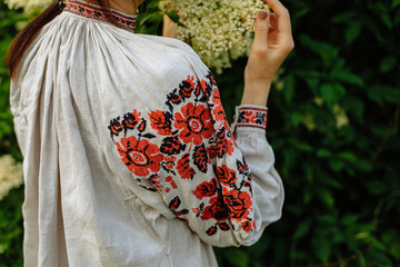 A girl in a national dress poses in a field among green bushes and trees