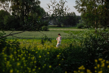 A girl in a national dress poses in a field among green bushes and trees