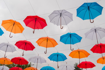 Obraz premium Low angle view: colorful umbrellas hanging against gray overcast sky and swaying in wind at summer city festival. Street decoration, celebration, art, holiday concept