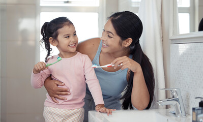 Mother with girl learning to brush teeth with toothbrush together in bathroom for oral or dental...