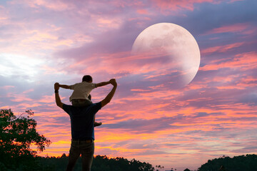 Happy Dad carrying son on shoulders looking future project with the Moon. Silhouette of father and son.