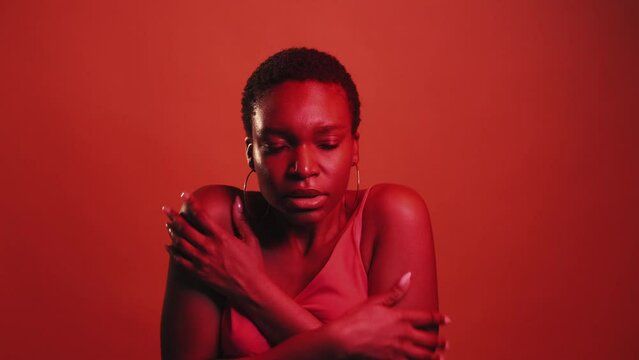 Cold gesture. Chilly weather. Flu fever. Red neon color light shivering freezing sick woman embracing shoulders keeping warmth isolated on dark bright gif loop boomerang animation.