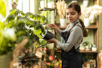 Little girl watering flowers in florist shop. - obrazy, fototapety, plakaty