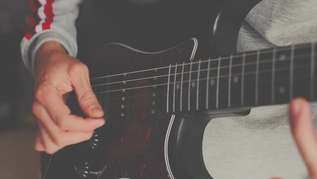 Strumming acoustic guitar. Musician plays music. Man fingers holding mediator. Man hand playing guitar neck in dark room. Unrecognizable person rehearsing, fretboard close-up.
