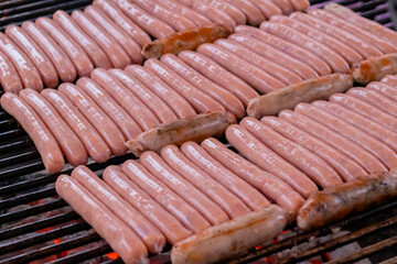 Process of grilling fresh meat sausages on big round grill at summer local food market - close up view. Outdoor cooking, barbecue, gastronomy, cookery, street food concept