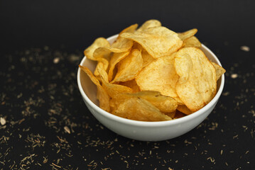 White ceramic bowl with golden potato chips on a black background.