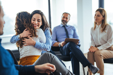 Portrait of female psychologist embracing young woman during therapy session in support group. Side...