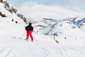 Fototapeta na wymiar Defying the slope: an unrecognizable person with his back turned in red clothes skiing on the mountain. winter sports. 