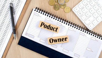 PRODUCT OWNER word written on wooden block on planner with coins, clipboard and a calculator