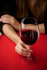 A woman holding a glass of red wine. Close-up of a glass of red wine against a red tablecloth