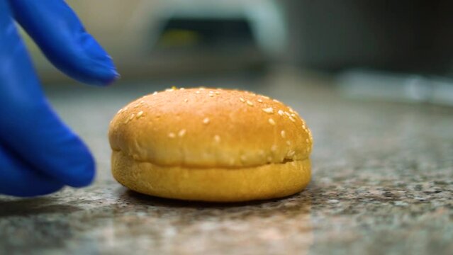 Hands with blue gloves put burger bun on the table, making hamburger