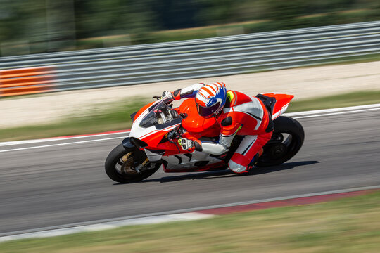 A motorcycle rider riding on an white,orange sport motorcycle through a corner at high speed. Leaning from the bike and dragging a knee. 
