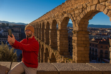 Young man taking a photo with his mobile phone next to an ancient Roman aqueduct in a European city