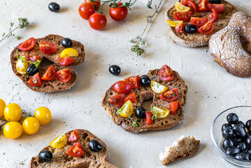 Fototapeta na wymiar Friselle are typical Italian twice-baked bread topped with red and yellow tomatoes, olive oil, olives and oregano on light sand background. Top view