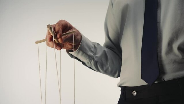 A businessman in a gray shirt and black tie controls a puppet with a wooden manipulator and strings. A puppeteer controls a doll marionette on a white isolated background. Close up.