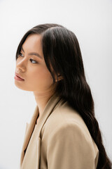 portrait of brunette asian woman with long hair and natural makeup looking away isolated on grey.