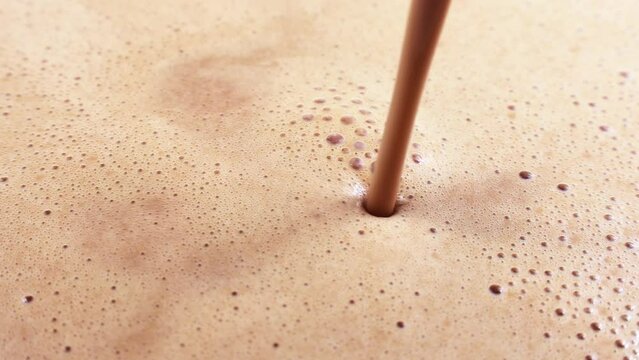 Brown foamy chocolate milk or milkshake with bubbles flowing close up
