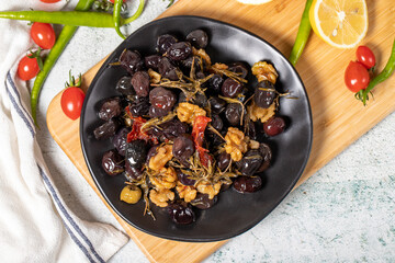 Mixed black olives. Special mixed olives prepared with dried red pepper, sun-dried tomatoes, thyme, walnuts and rosemary on a wooden serving plate. Top view