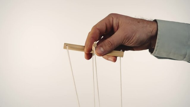 The hand of a man in a gray shirt controls a puppet using a wooden manipulator and strings. Hand handling at puppet by pulling strings to make the character move. White background. Close up.