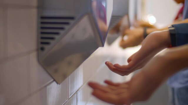 Cropped shot of person using hand dryer in a public toilet or lavatory after washing hands. Realtime