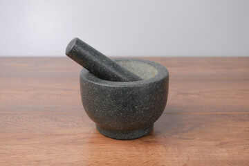 Black Stone granite mortar and pestle grinder on a wooden table with a grey background, 