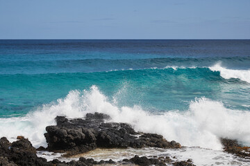 Wave braking ashore with volcanic rocks in foreground and sea and sky in the background