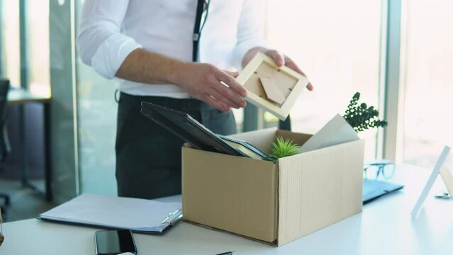 Employee putting his stuff from work desk in carton box, leaving job, close up