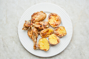 Chicken baked in pieces with potatoes and onion on a white dish. Home cooking. Healthy food, cooked without oil and salt.