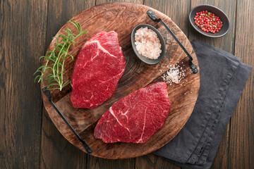 Raw beef steak. Marbled raw fresh Ribeye steak with rosemary, salt and pepper on cutting board on dark concrete background. Raw beef steak and spices for cooking.