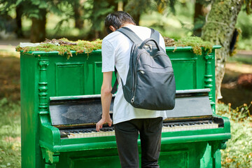 Young guy teenager plays classic music on piano, interactive outdoor art object in public park,...