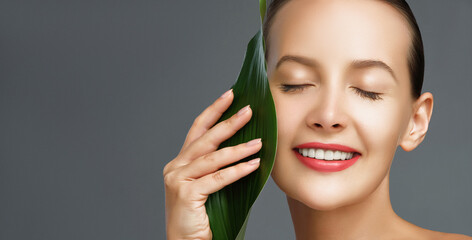 Organic skincare. Beauty face close-up portrait of a young woman posing with a green tropical leaf....