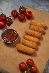 cheese sticks with breaded meat lie on a wooden board. with vegetables and decor around and sauce