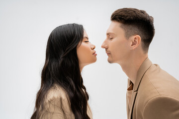 side view of stylish interracial couple standing face to face with closed eyes isolated on grey.