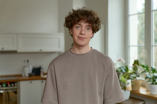 Photo people and lifestyle concept. Indoor shot of positive handsome young caucasian man with voluminous hair. An indoor portrait of a person smiling and looking at the camera, wearing casual clothing