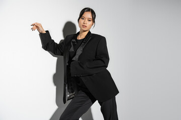 sensual asian woman in black elegant outfit looking at camera on grey background with shadow.