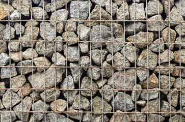 stones behind metal grate. Granite paving stone in steel container. metal mesh holds wall of stones.