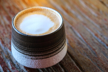 Hot latte coffee in a round mug on an old wooden table with warm light and copy space